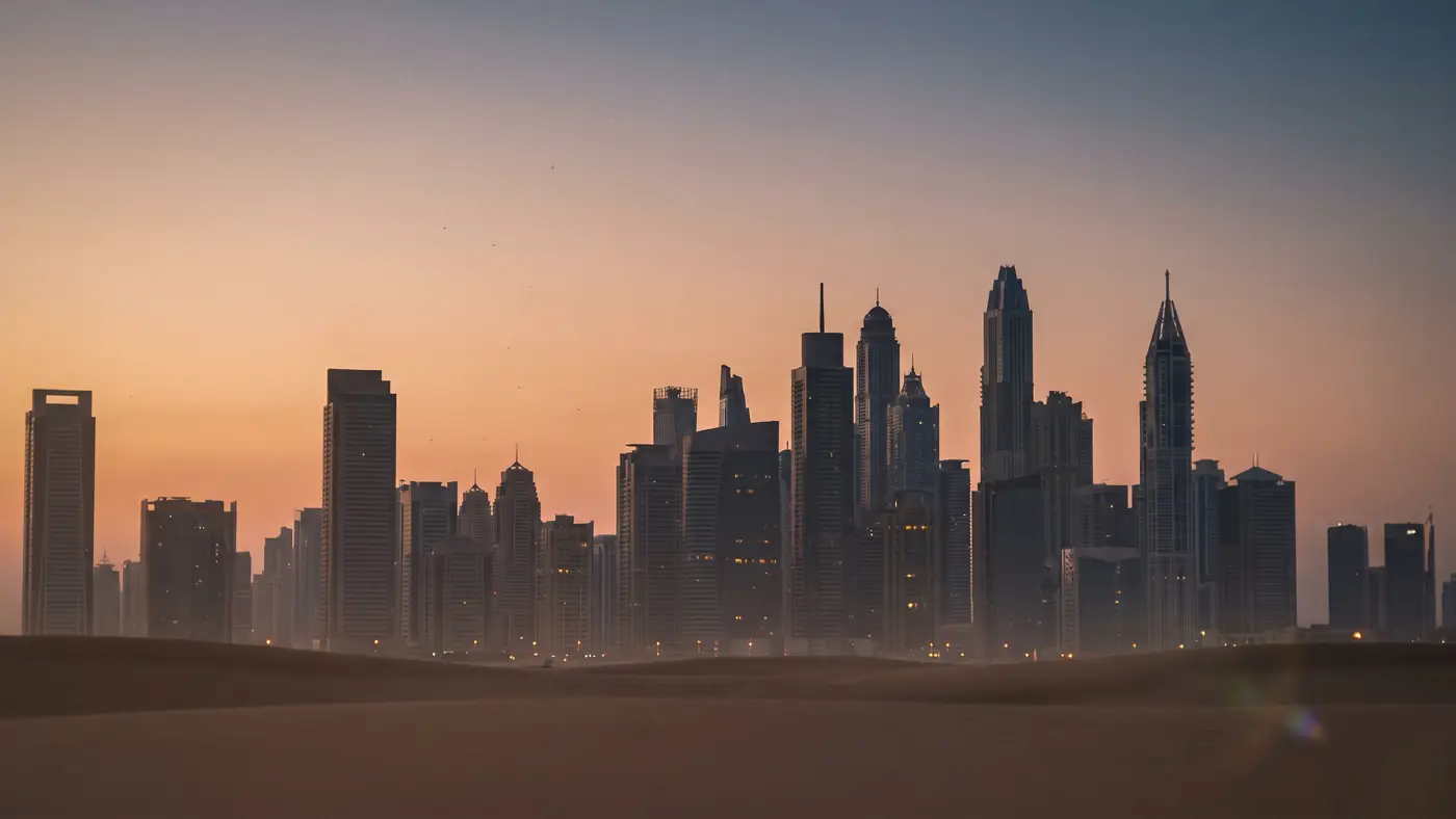 A clean modern desert-city skyline of contemporary towers silhouetted against a warm dusk sky.